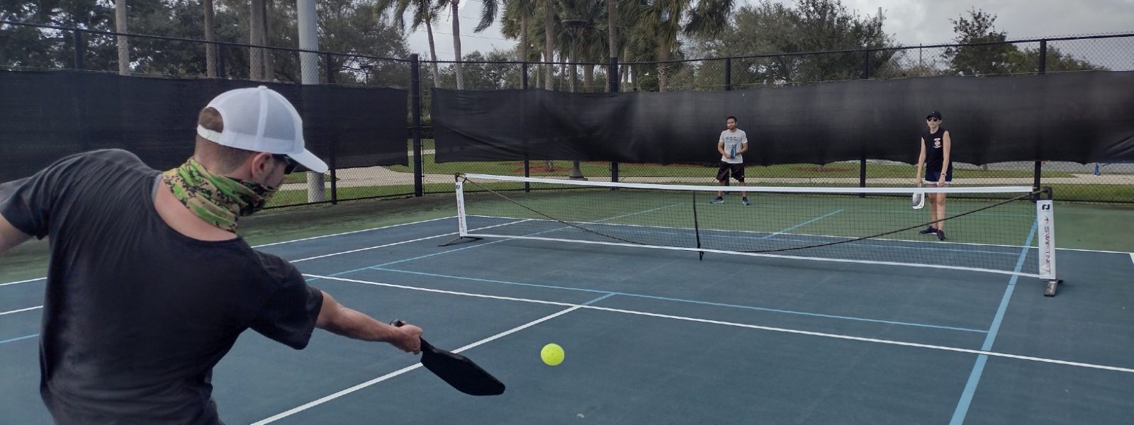 Pickleball player about to serve to the other team with cloud in the sky on a pickleball court